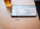 A cell phone sitting on top of a wooden table next to a beer.