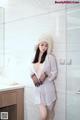 A woman in a white shirt and hat standing in a bathroom.