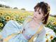 A woman in a blue dress sitting in a field of sunflowers.