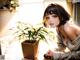 A woman sitting on a bed next to a potted plant.