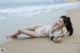 A woman in a white bikini laying on the beach.