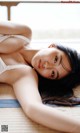 A woman laying on top of a bed in a white bra.